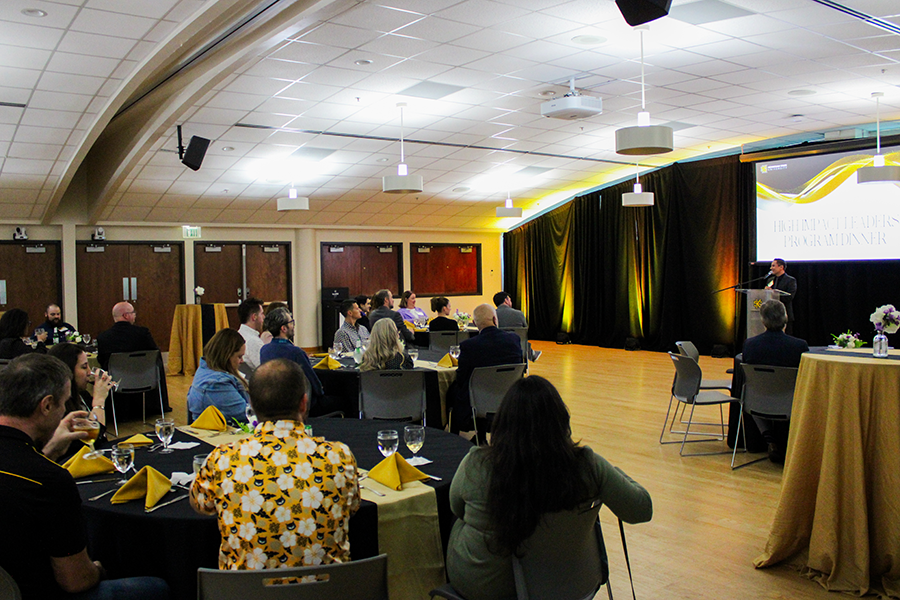 HILP Dinner 2025-2026 / A group of people seated at round tables in a banquet hall with wooden floors, white ceilings, and soft lighting. Some tables have yellow napkins and flower centerpieces, creating a formal event atmosphere.
