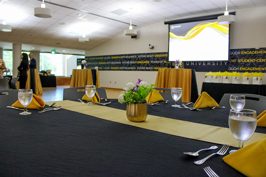 HILP Dinner 2025-2026 / Elegant banquet setup with black and gold accents, featuring neatly arranged tables with yellow napkins and floral centerpieces. A presentation screen is visible in the background.