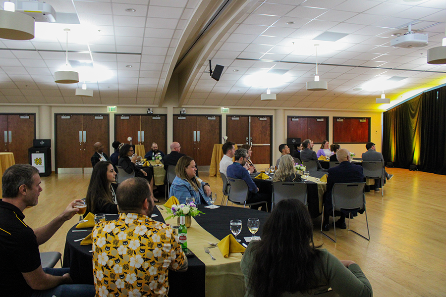HILP Dinner 2025-2026 / A speaker addresses an attentive audience in a conference room. The room is dimly lit, creating a focused, formal atmosphere. Attendees sit at round tables.