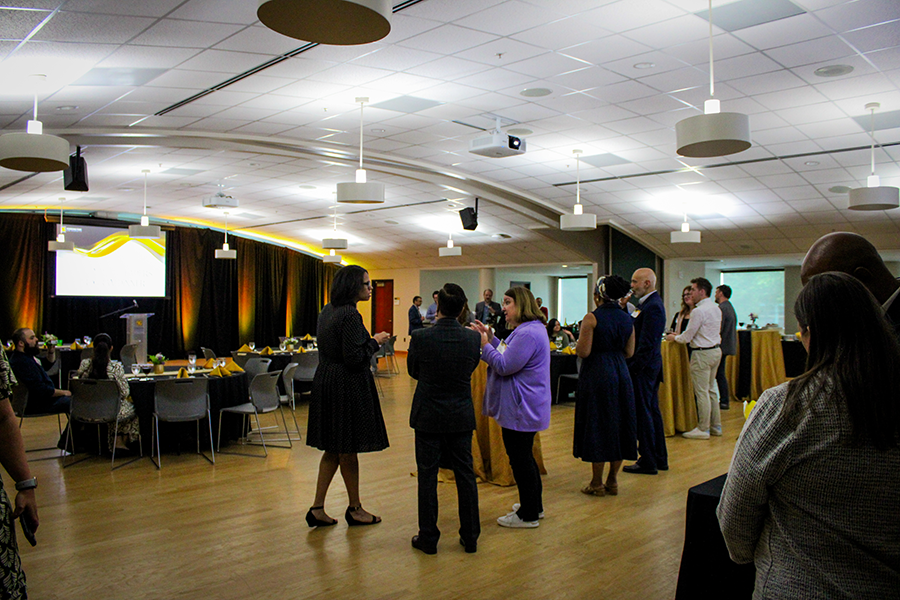 HILP Dinner 2025-2026 / A group of people in formal attire converse in a spacious, well-lit banquet hall with round tables. The atmosphere is lively and social.