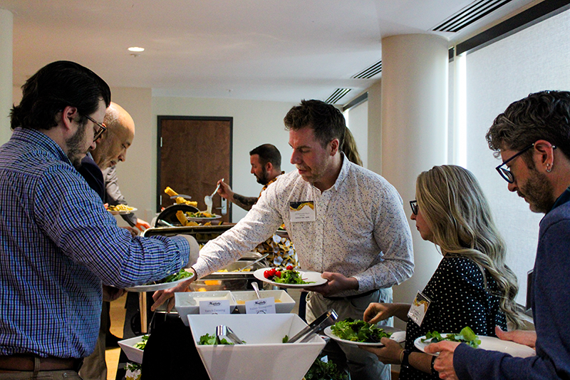 HILP Dinner 2025-2026 / People serve themselves at a buffet in a well-lit room. The atmosphere is casual and social, with bowls of salad and various dishes available.