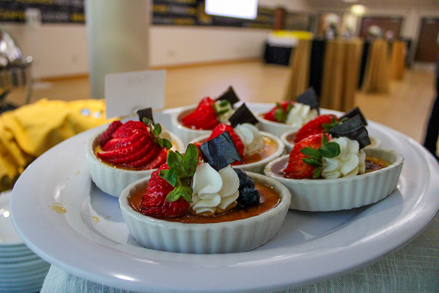 HILP Dinner 2025-2026 / White ramekins filled with crème brûlée, topped with strawberries, whipped cream, and chocolate pieces on a white plate. Sophisticated dessert setting.