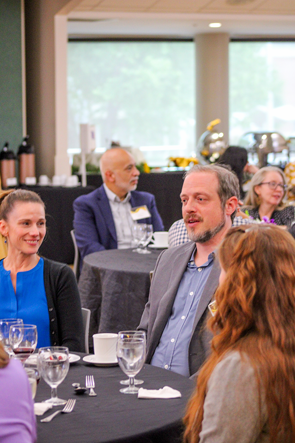 HILP Dinner 2025-2026 / People sit at round tables covered with black cloths in a well-lit room, chatting and smiling. The atmosphere is lively and social, with drinks and silverware visible.