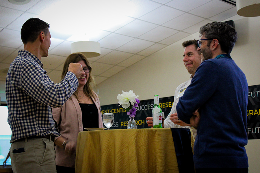 HILP Dinner 2025-2026 / Four people engage in lively conversation around a table with flowers and drinks. The setting is casual, with laughter and friendly interaction.