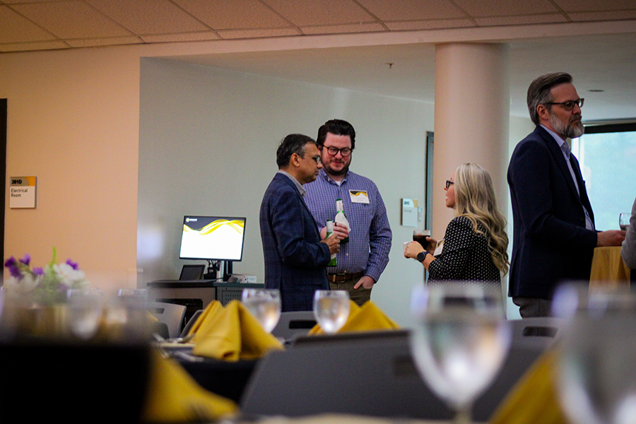 HILP Dinner 2025-2026 / A small group of people in business attire engage in conversation at a social event. The setting includes decorated tables, creating a professional yet relaxed atmosphere.