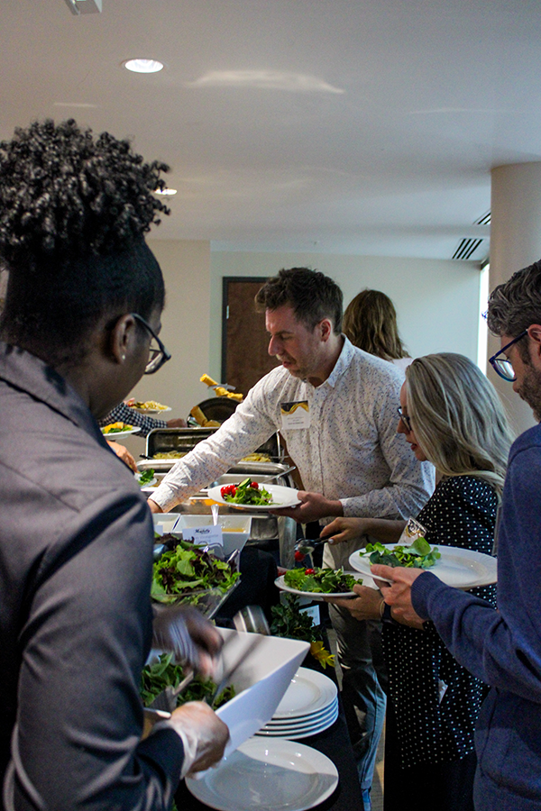 HILP Dinner 2025-2026 / A group of people at a buffet serving themselves salads. They seem focused and engaged, creating a lively and social atmosphere.