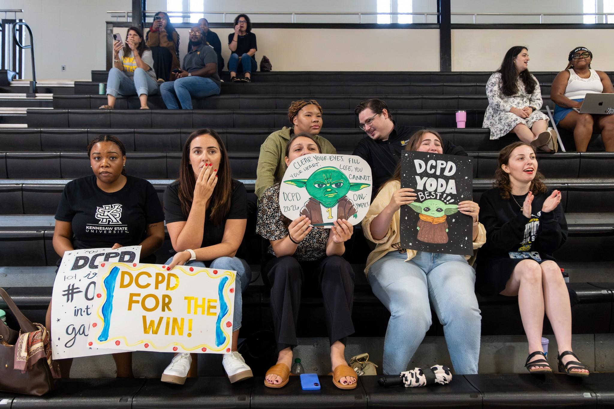 2026 Owlympics / Owlympics spectators holding home made signs cheering on their team from the bleachers.