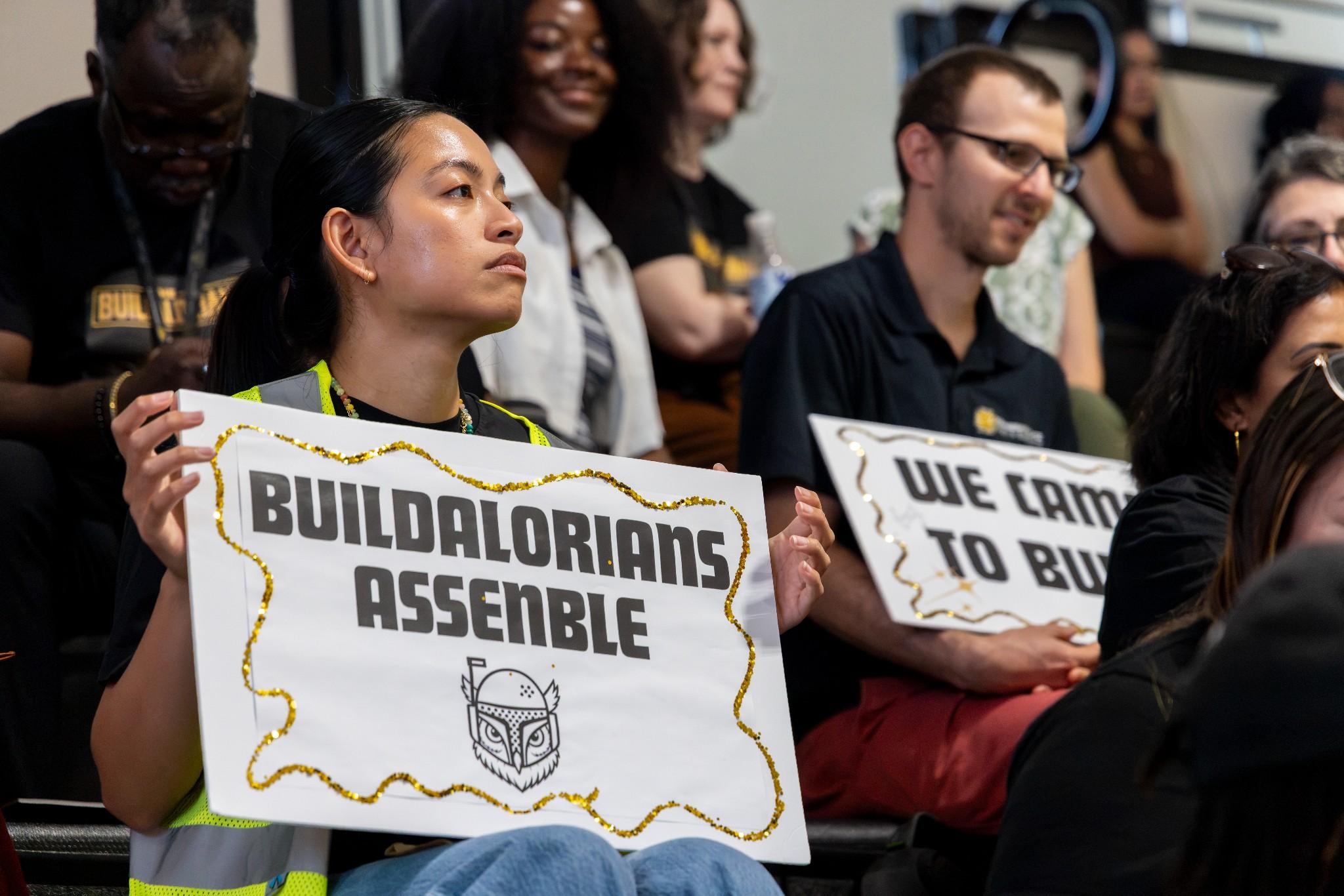 2026 Owlympics / Spectator at owlympics holds handmade signs reading “Build a Lorians Assemble” 