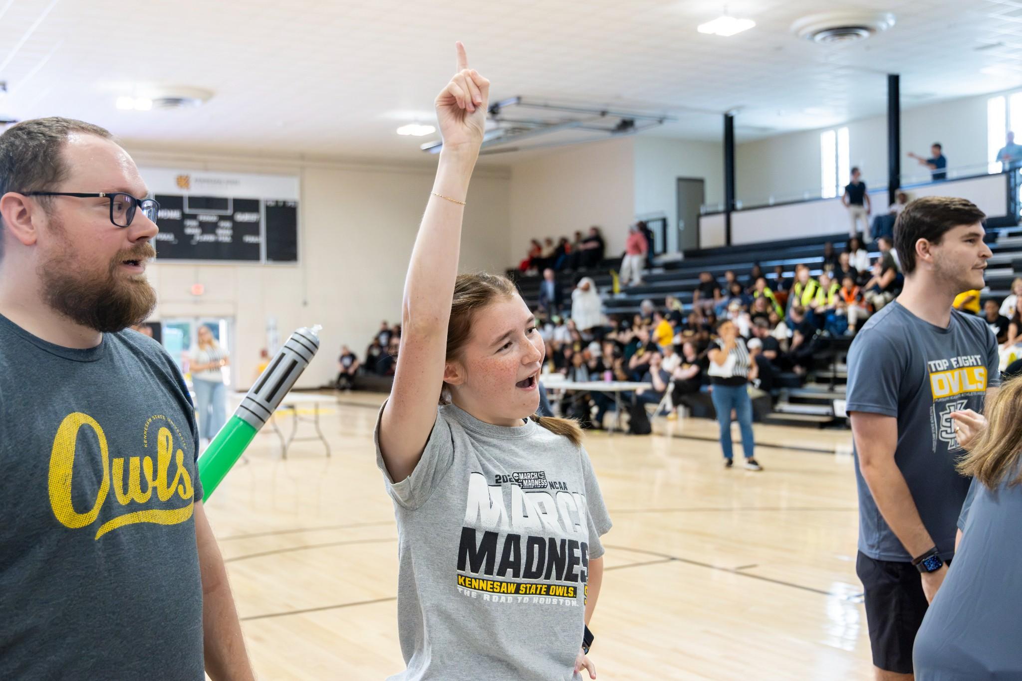 2026 Owlympics / Woman cheers on teams holding up fingers indicating "number 1".
