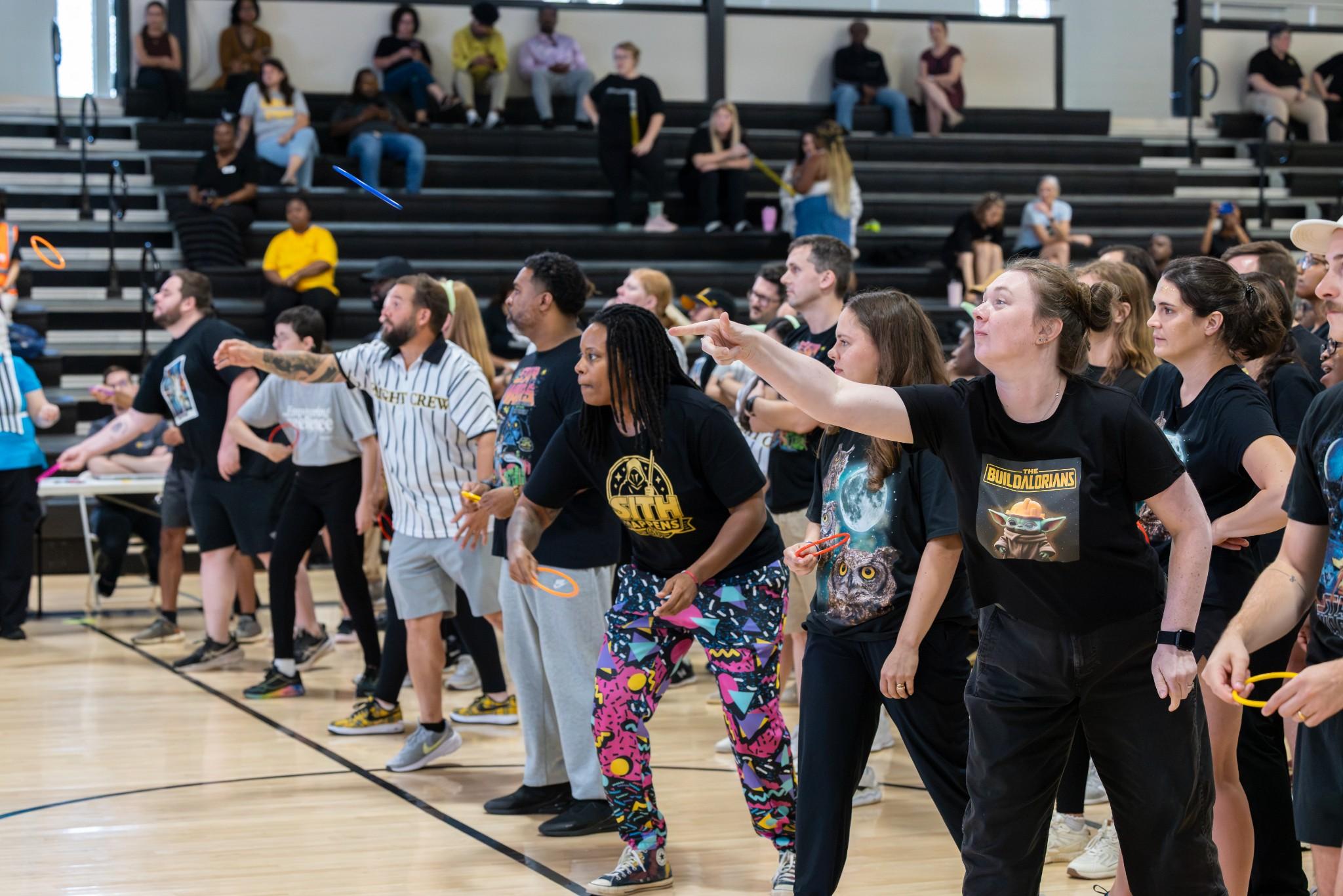 2026 Owlympics / A diverse group plays a lively gymnasium game, pointing and moving together while spectators watch from the bleachers.