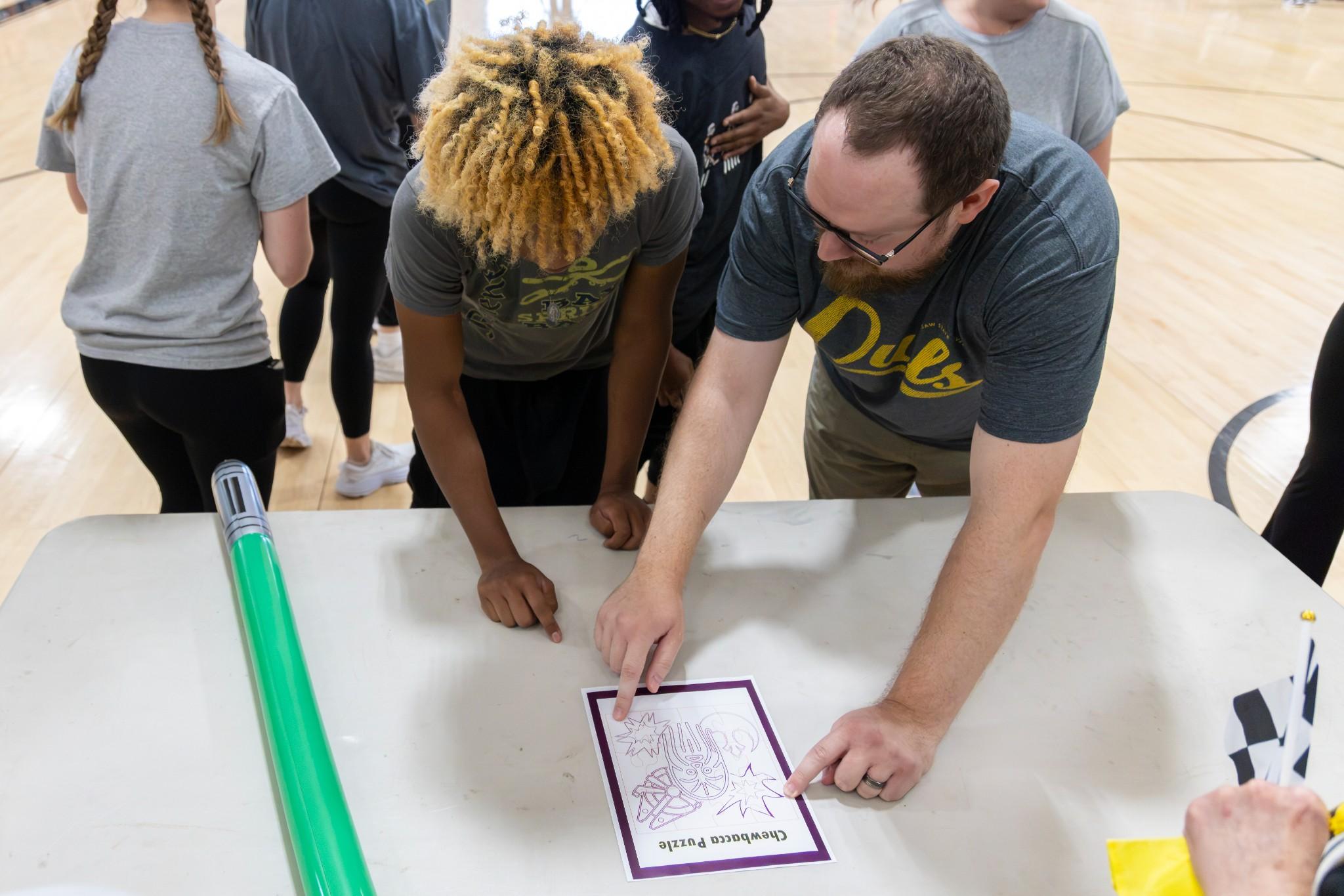 2026 Owlympics / Team members lean over a gym table, studying a worksheet together before the next round of games.
