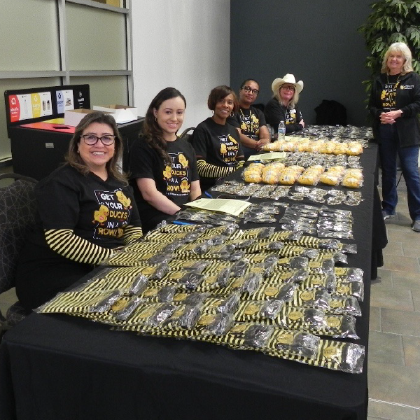 KSU fair with A group of women in matching shirts sit at a table covered with bags of cookies, displaying a cheerful and welcoming atmosphere.