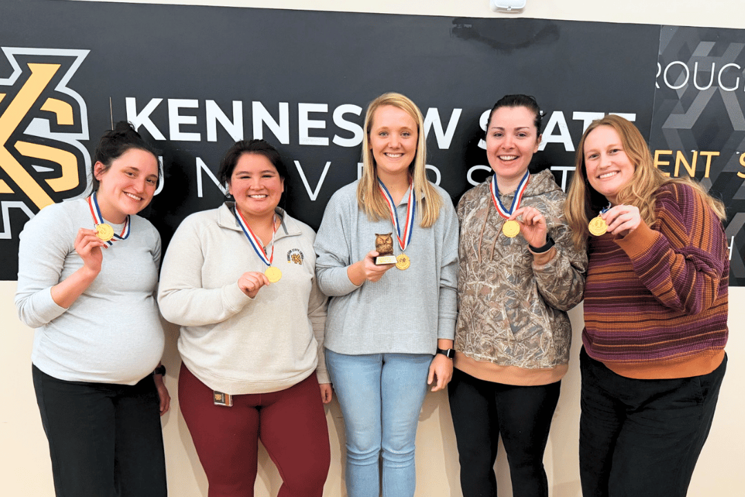 first place marietta trivia winners wearing their gold medals and holding up the coveted owl trophy. They are all smiles.