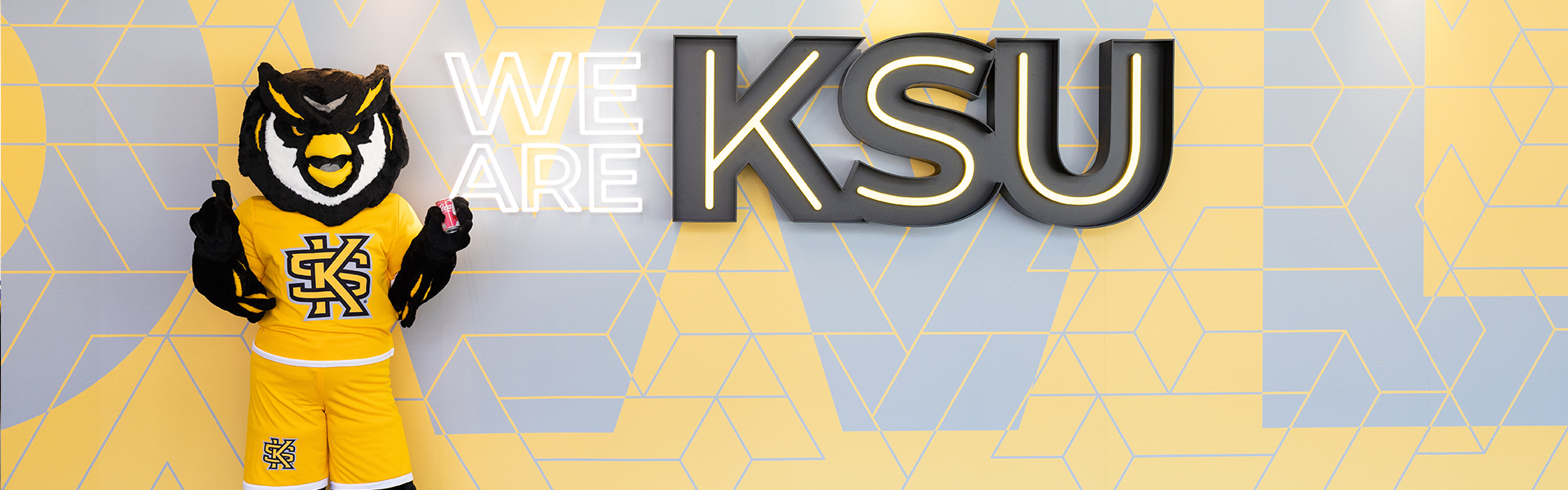 scrappy standing in front of the "we are ksu" sign.