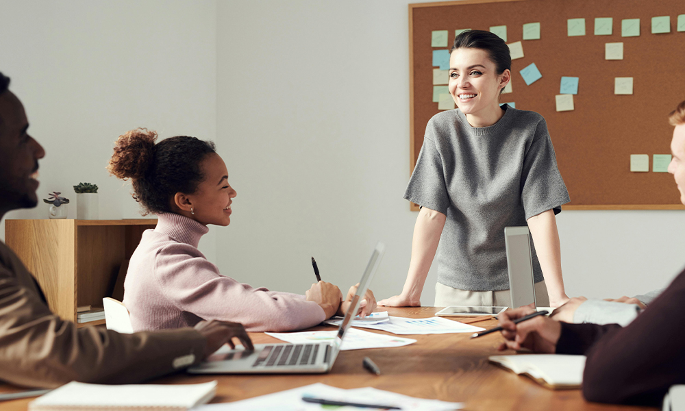 group of business professionals in meeting smiling with laptop, pen and papers on desk