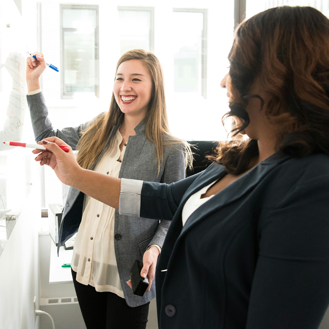two females smiling while writing on board