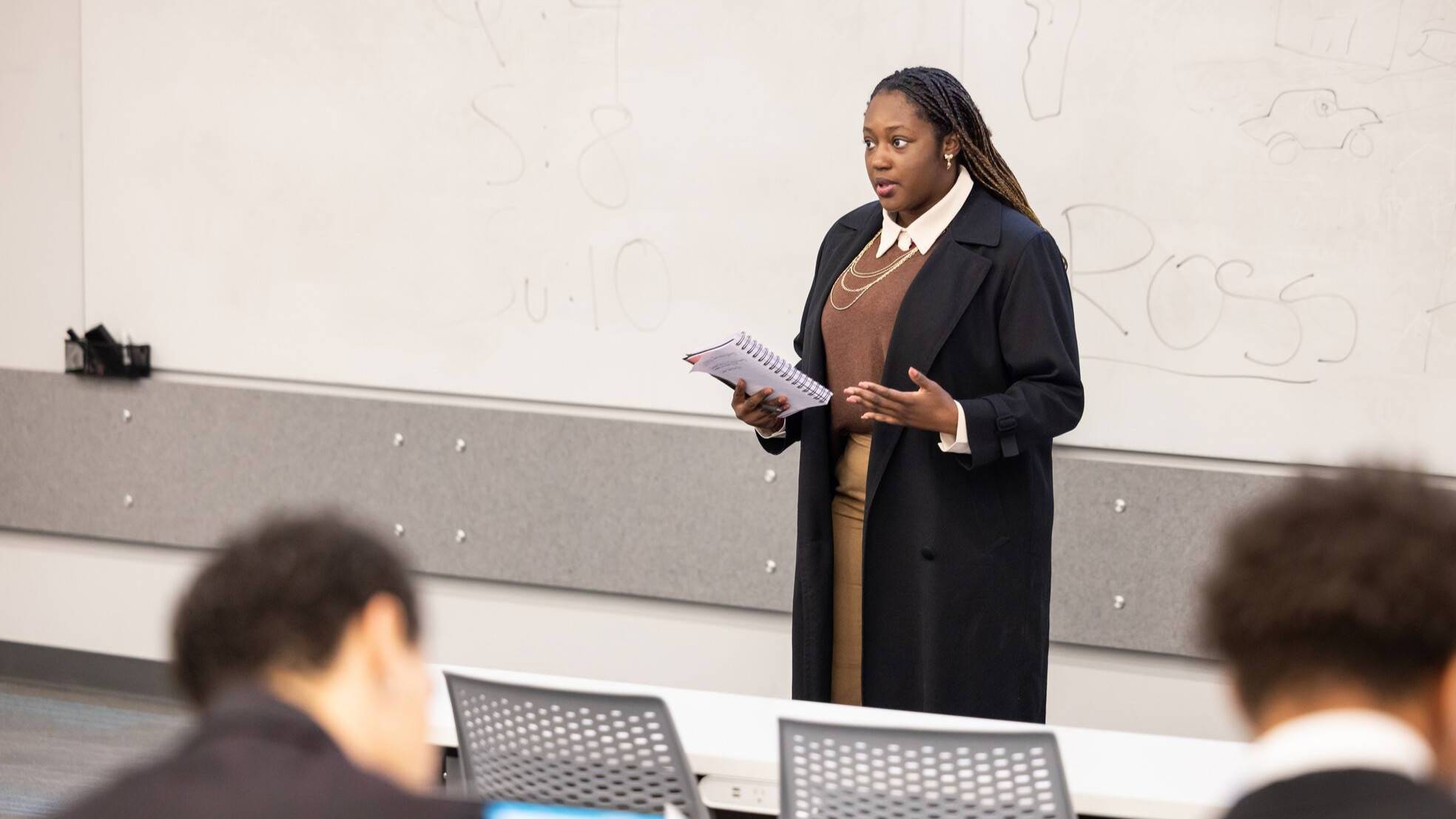 a woman speaks at the front of a classrooom
