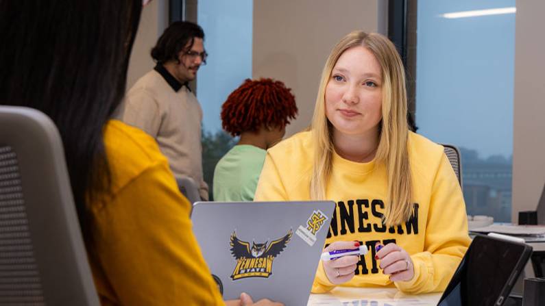 a woman sits and speaks with a KSU student