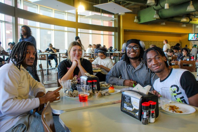 a group of 4 smiling students sitting at a table in the dining hall