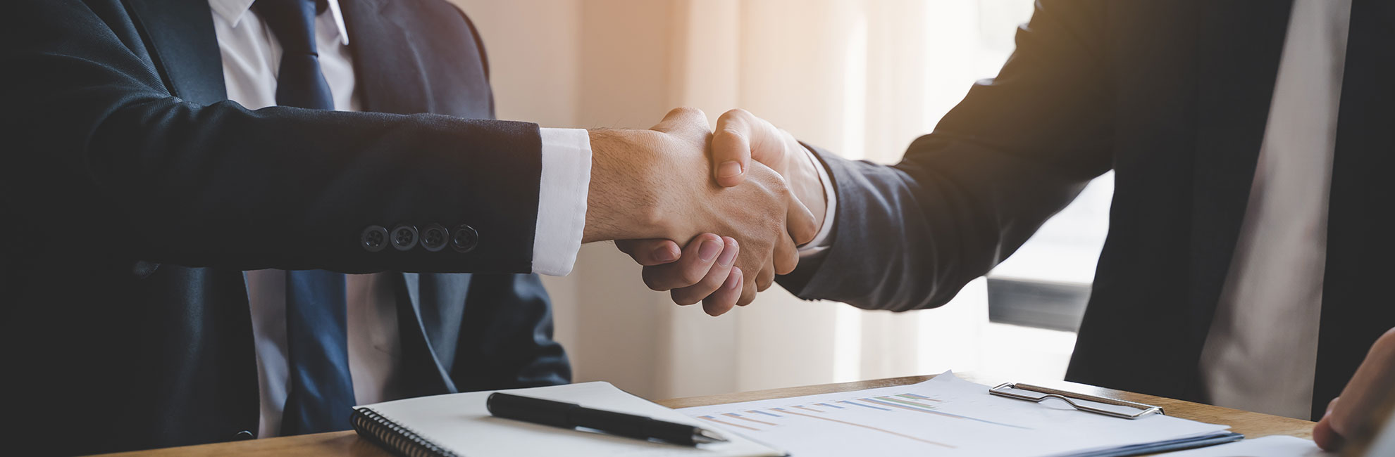 two guys in suits over table shaking hands
