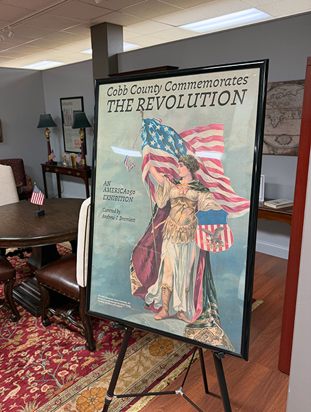 A framed poster on an stand. The poster says Cobb County Commemorates the Revolution.