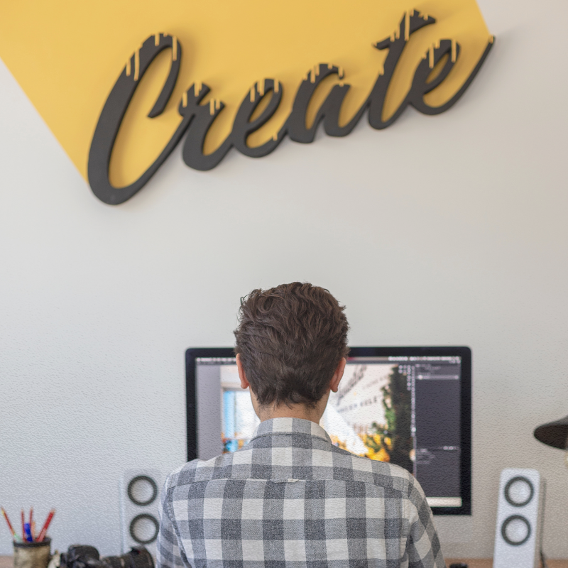 guy in front of computer with the word create on the wall