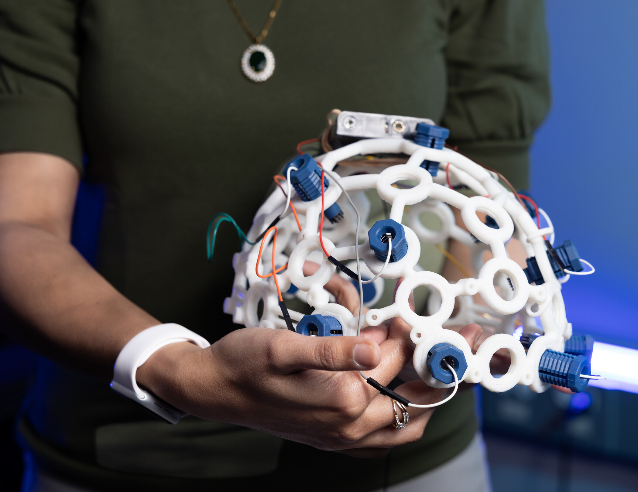 A person holds a white, circular 3D-printed device with blue sensors and wires.