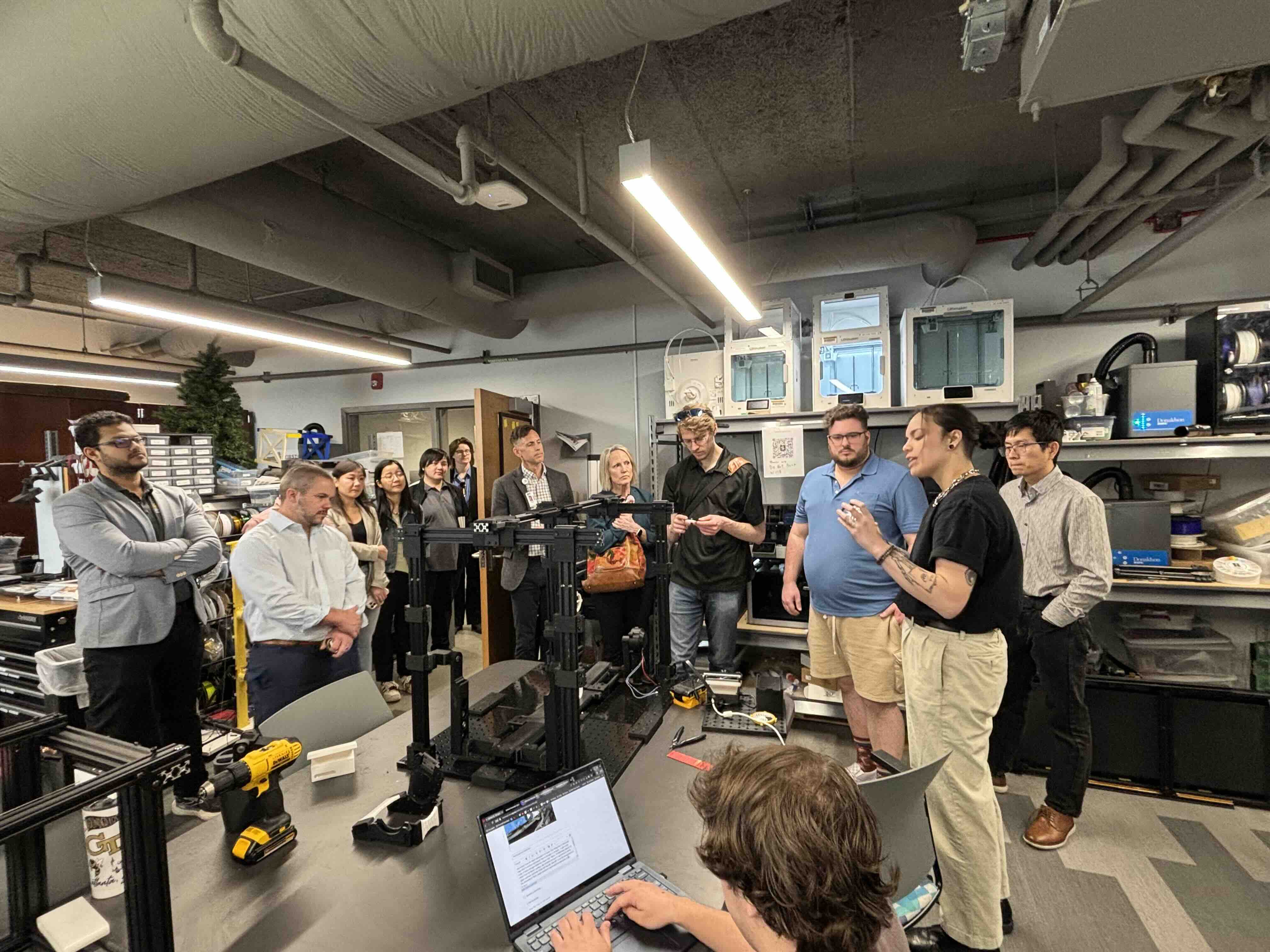 Student speaks at the head of room to a crowd of people. Setting is an engineering research lab.