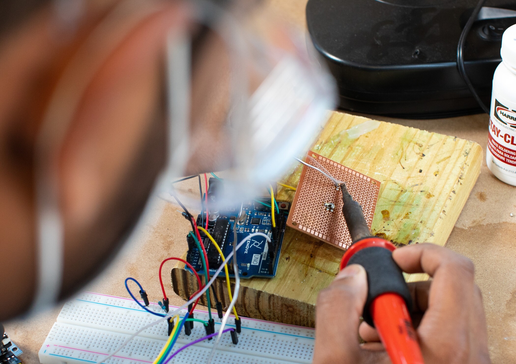 Person soldering a perforated circuit board connected to an Arduino Uno and breadboard.