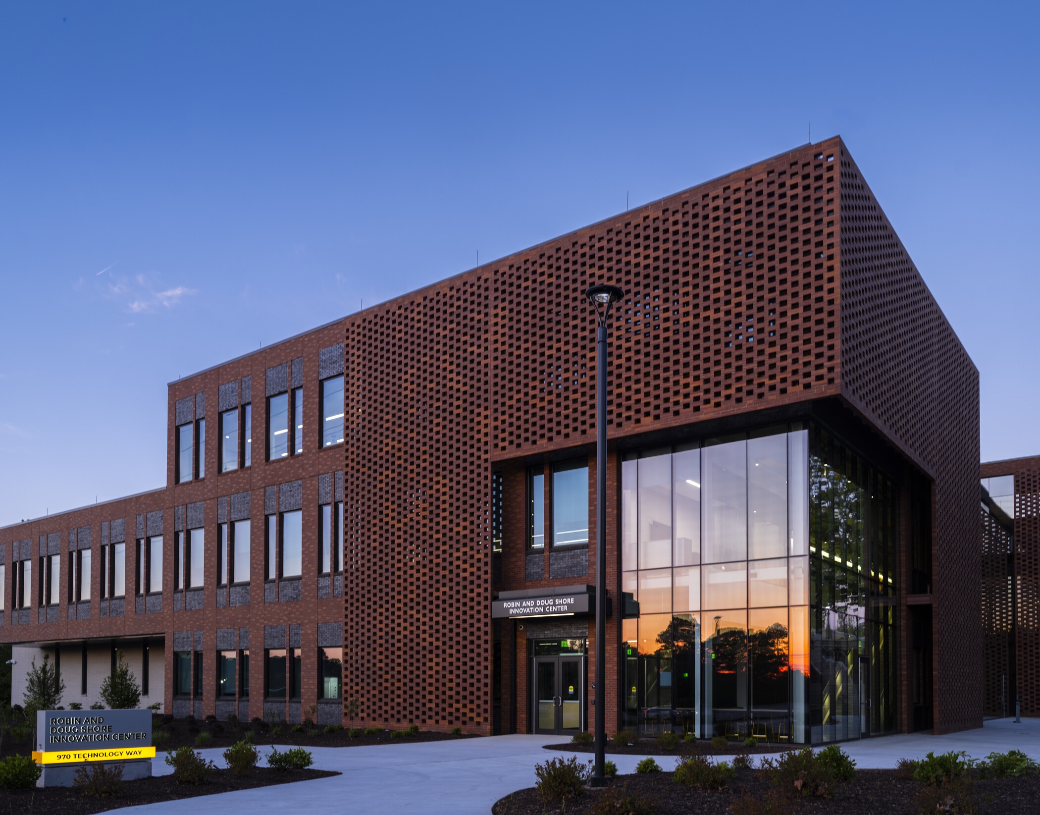 Exterior view of the Robin and Doug Shore Innovation Center, a modern red-brick building with patterned walls, large windows, and landscaped walkways.