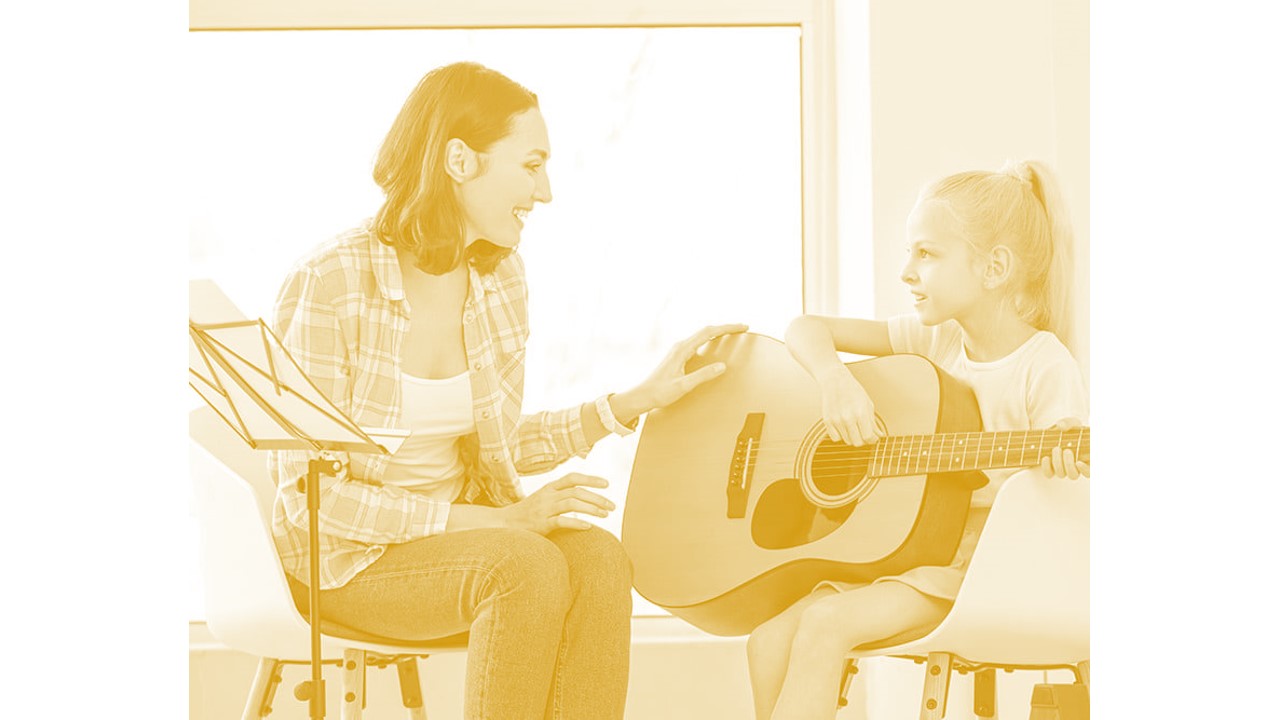 adult showing child how to play guitar