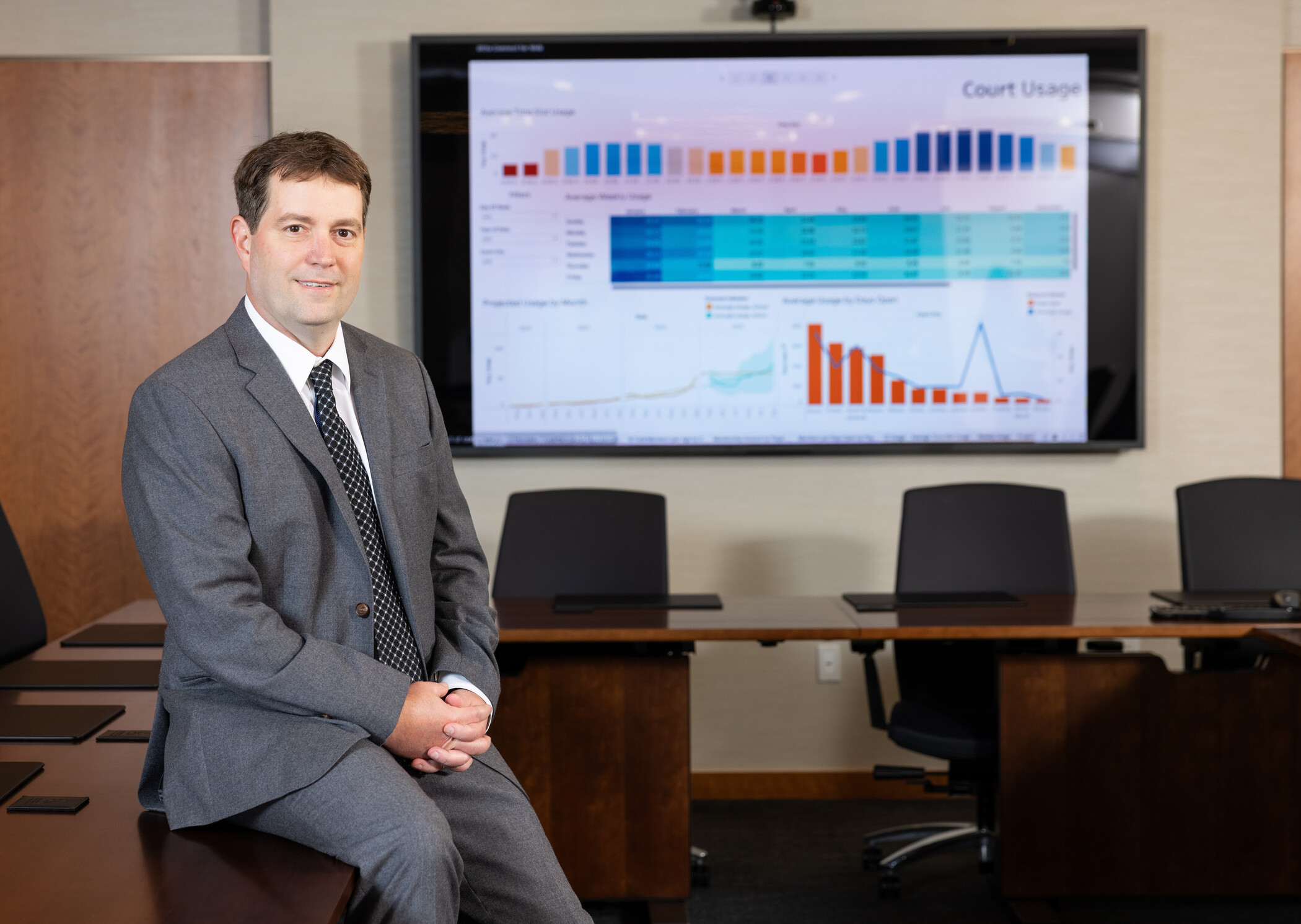 researcher sitting on table in front of tv screen showing graphs.