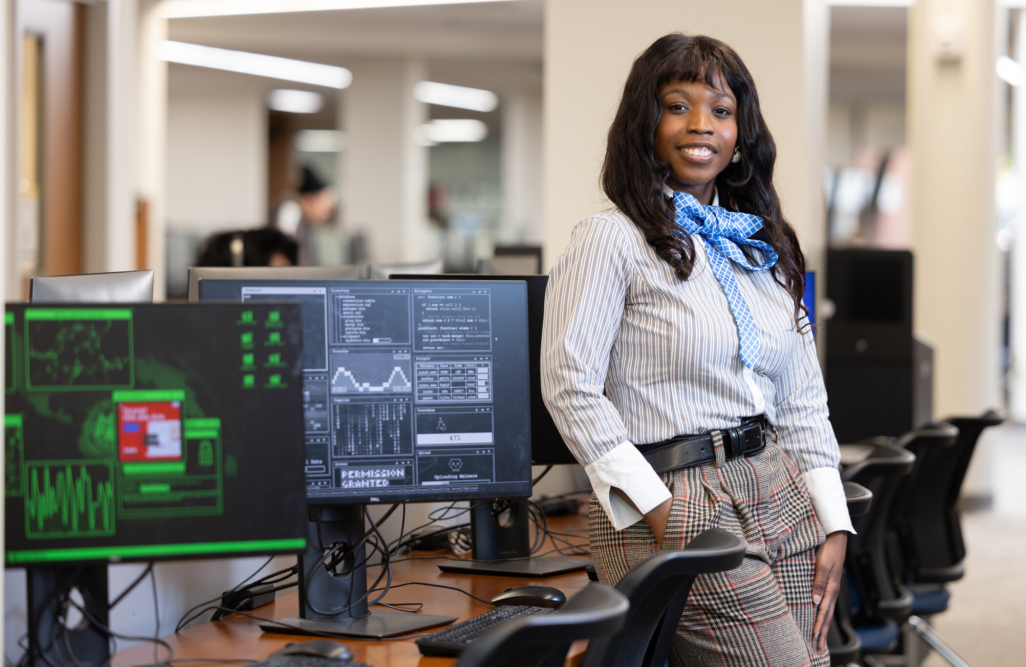 a researcher leans against a computer next to a computer screen showing data.