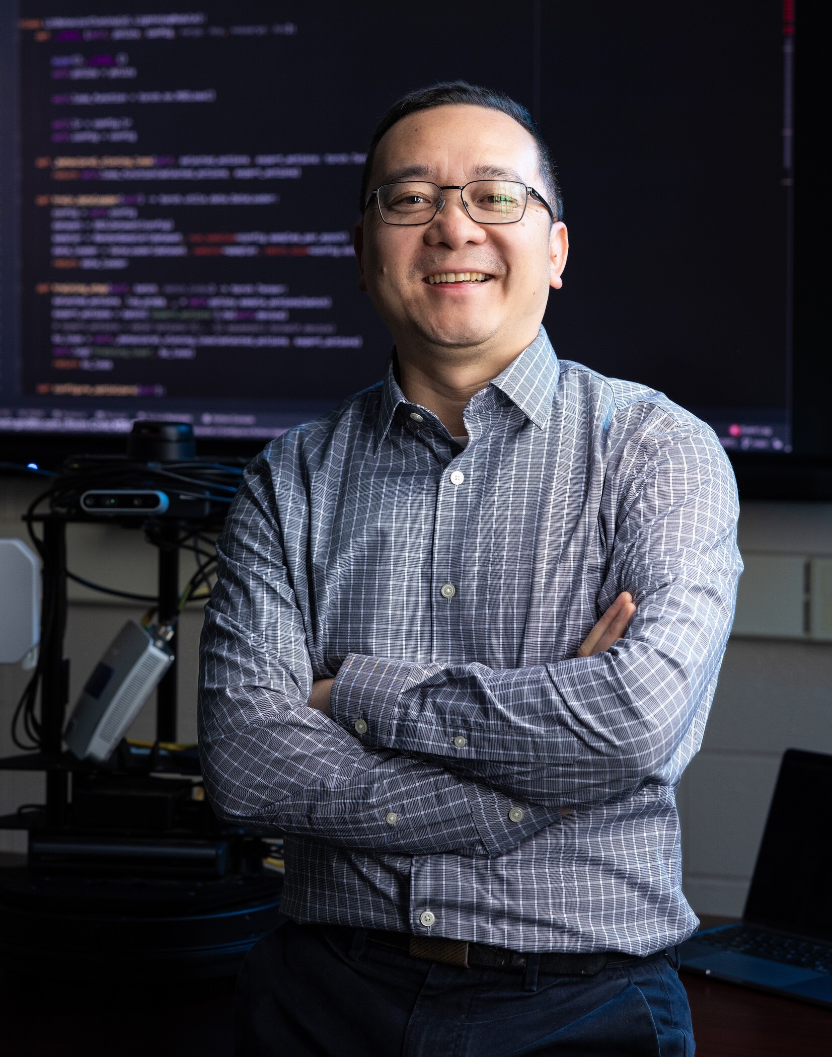 researcher with folded arms in front of screen showing code.