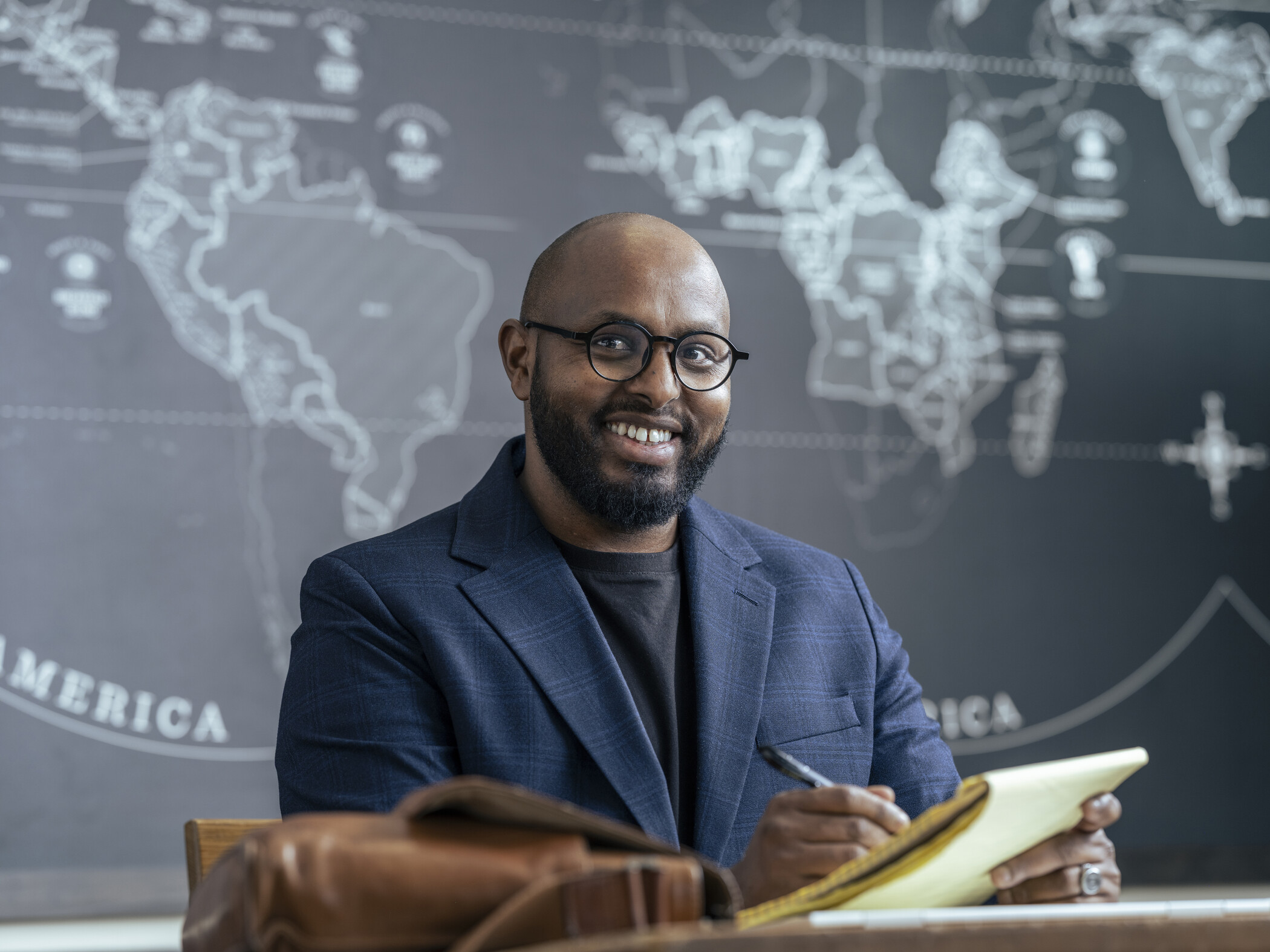 researcher sitting at table and holding legal pad in front of map of the world.