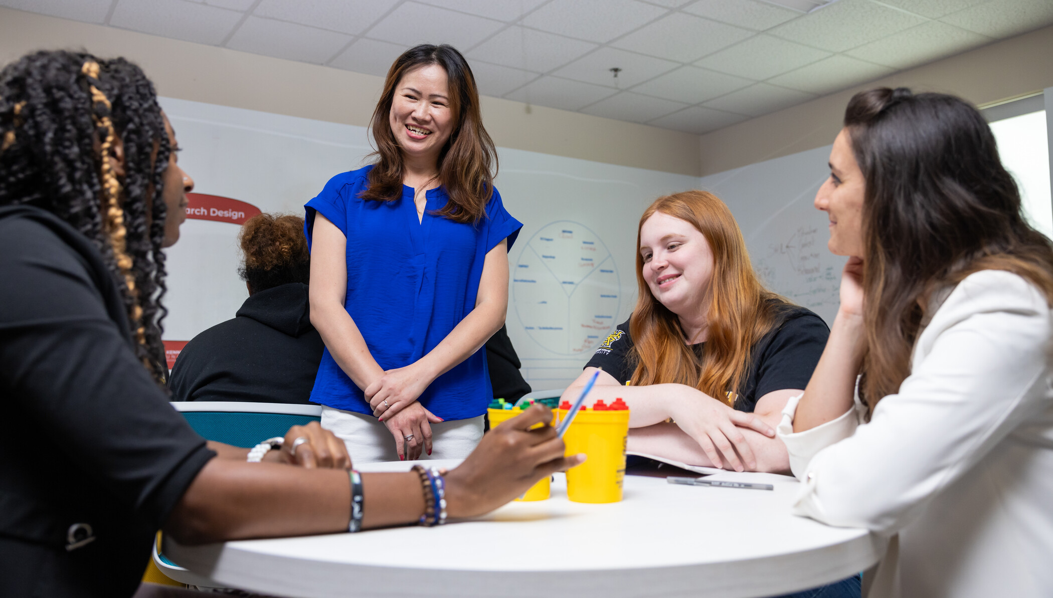 researcher standing at table with three people seated.