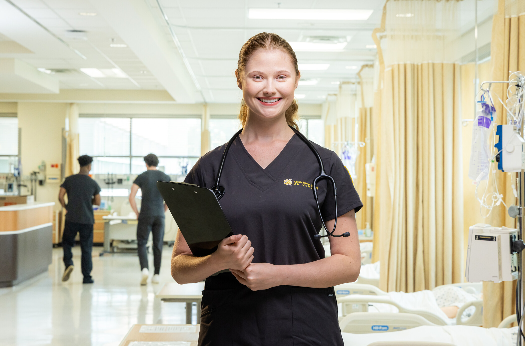 nurse standing in foreground of photo in nursing simulation lab.