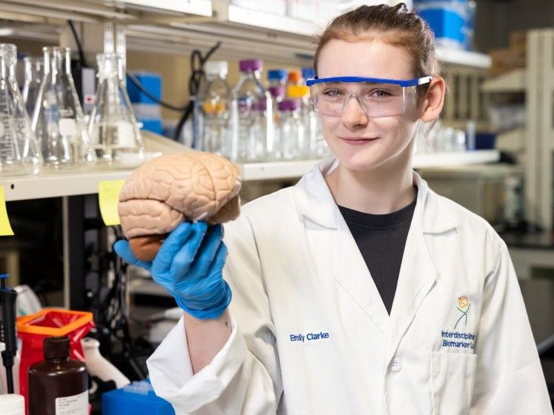 Student in lab coat holding a brain model in a research lab
