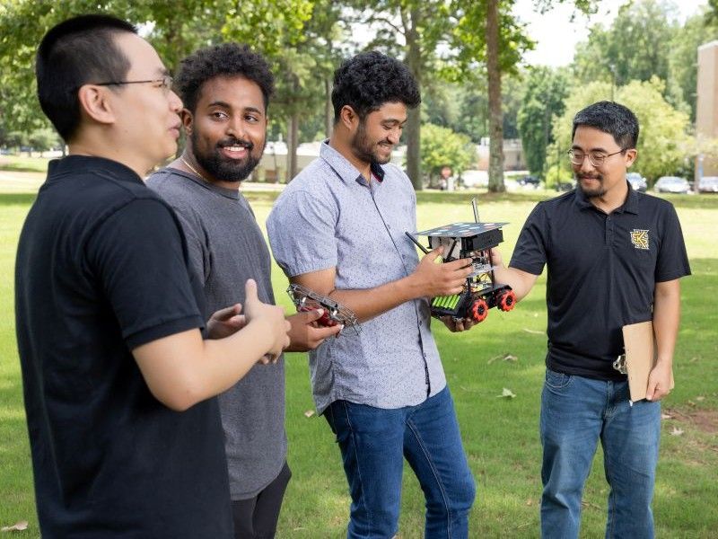 Students and faculty discussing a robotics project outdoors on campus