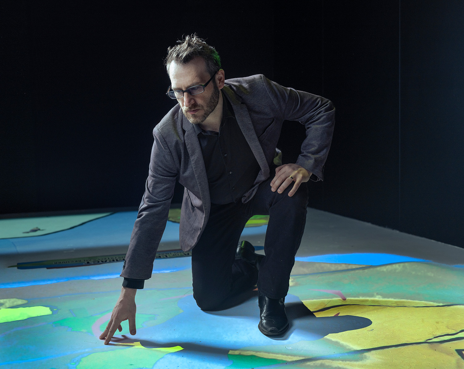 man in suit and glasses kneeling on floor