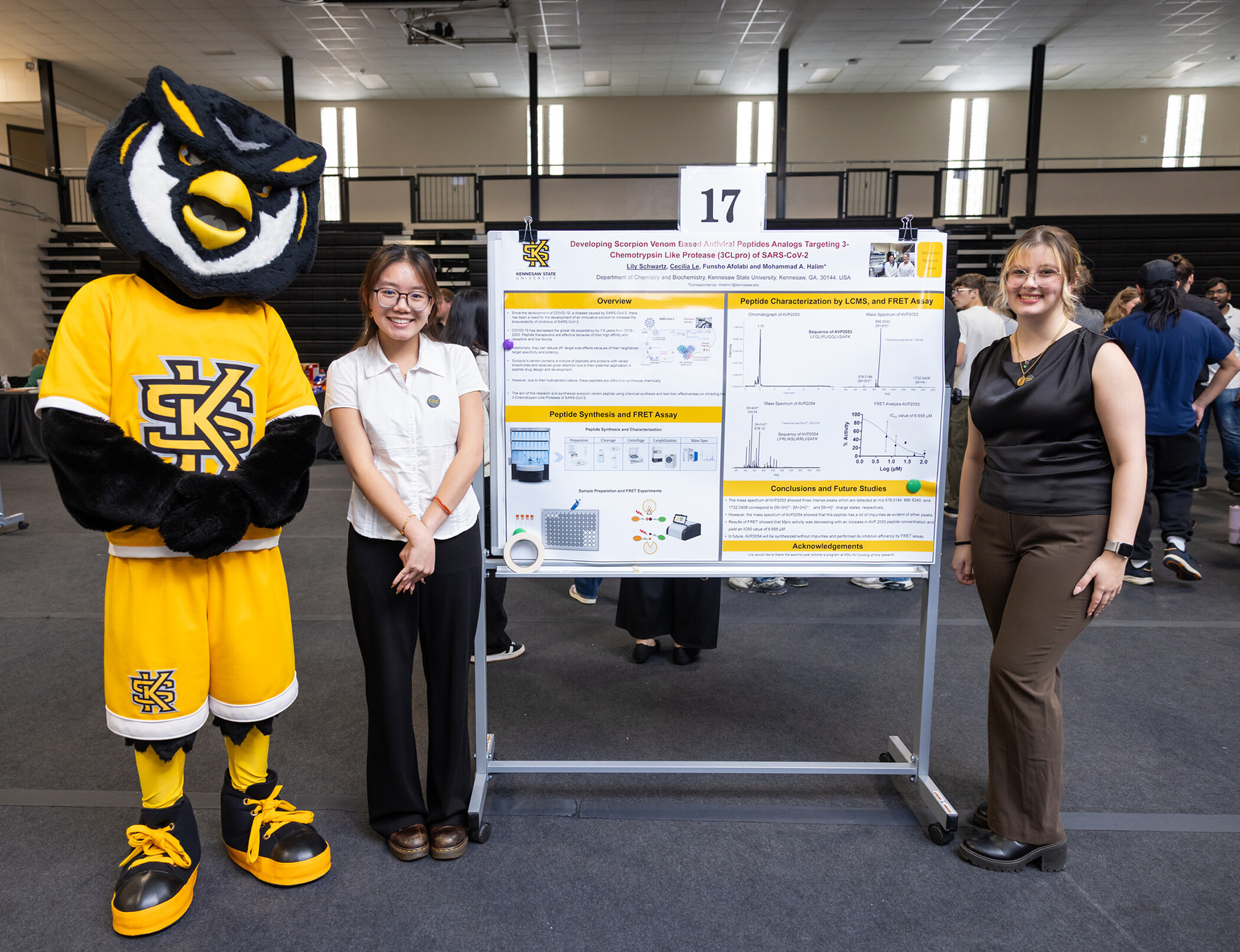 Kennesaw State University's mascot, Scrappy, stands next to two individuals in front of a research poster at an academic event.