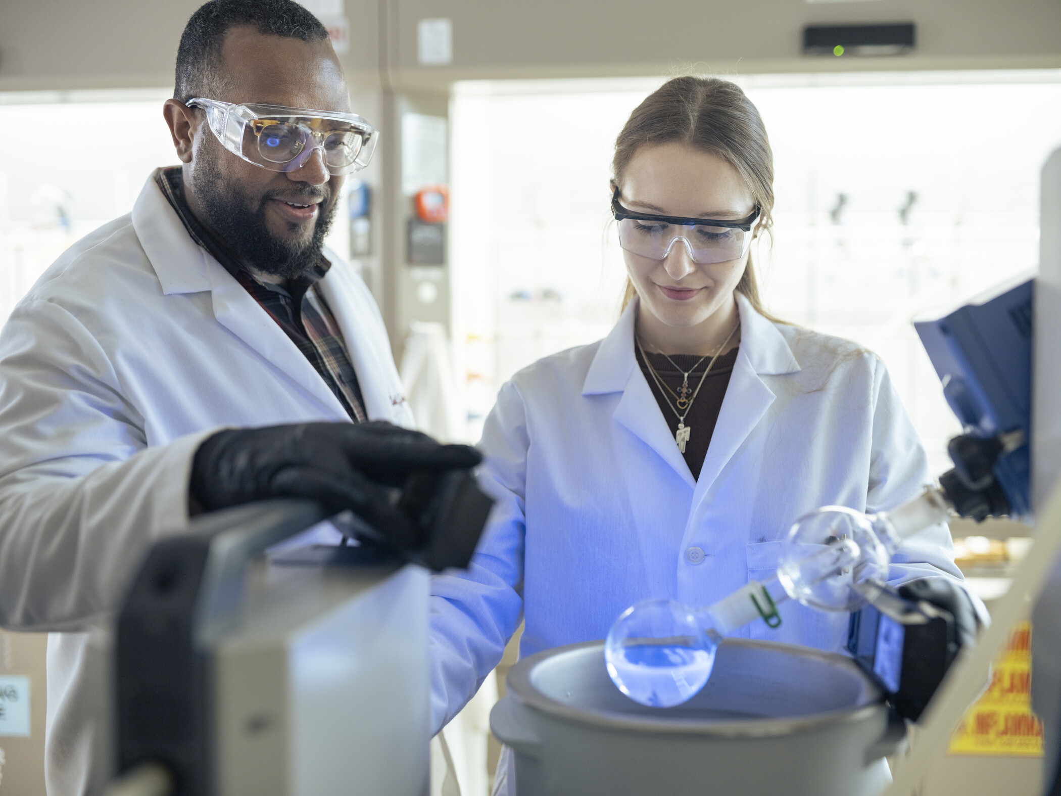 Two researchers in lab coats focused on a task, surrounded by lab equipment and materials in a research lab