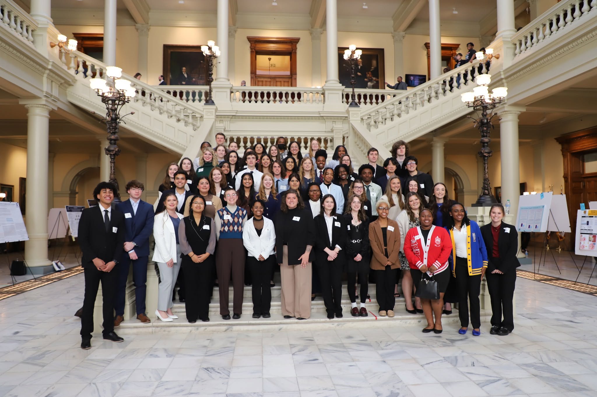 The image depicts a large group of people arranged on the steps of a grand staircase inside the Georgia Capitol building.