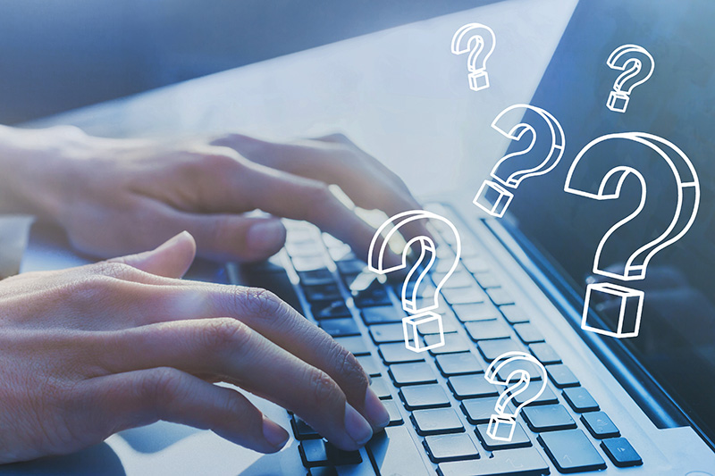 Hands typing on a laptop keyboard with question marks floating above.