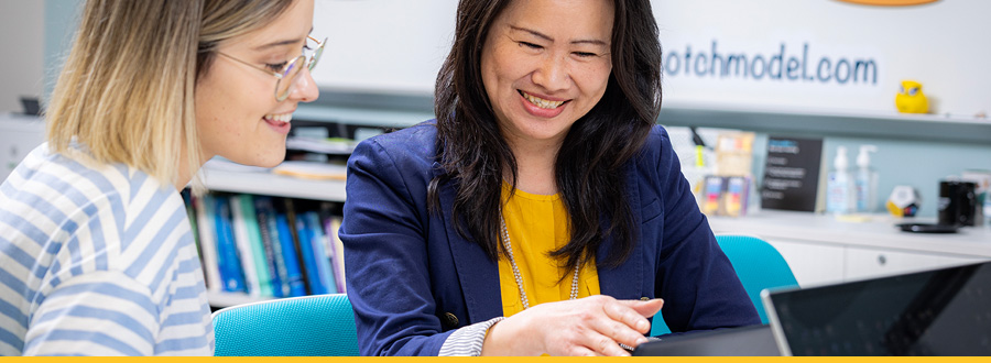 Two women are seated at a table, working together on a laptop, sharing ideas and insights.