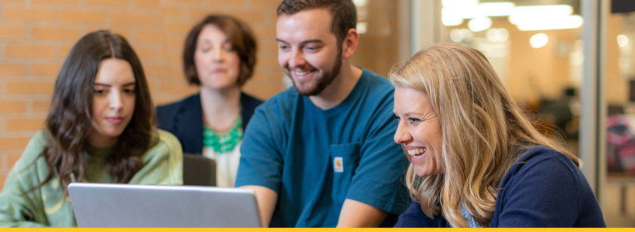 Two women sit at a table, focused on a laptop, engaged in conversation and collaboration.